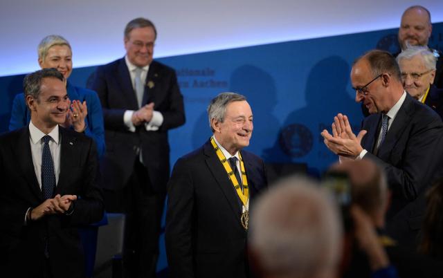 The former President of the European Central Bank (ECB) and former Italian Prime Minister Mario Draghi (C) is applauded by Greek Prime Minister Kyriakos Mitsotakis (L), Belarusian street protest leader Maria Kolesnikova (2nd L), Germany's former leader of the conservative Christian Democratic Union (CDU) party Armin Laschet (3rd L), German Chancellor Friedrich Merz (3rd R), former ECB President Jean-Claude Trichet (2nd R) and Aachen's mayor Michael Ziemons (R, background) as he is awarded the 2026 International Charlemagne Prize of Aachen, on May 14, 2026 in Aachen, western Germany. (Photo by Sascha Schuermann / AFP)
