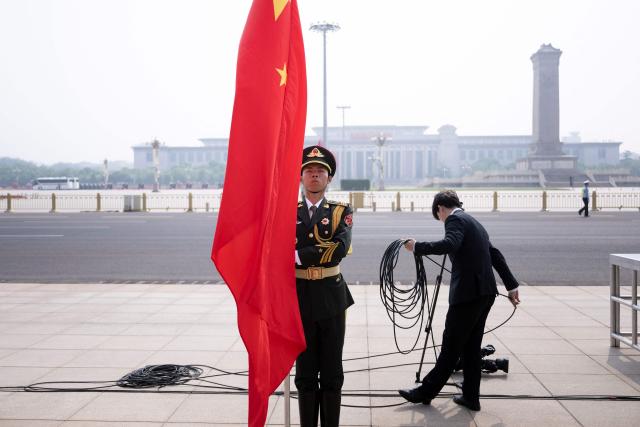 A member of the military waits to unfurl a Chinese flag as a staff member prepares for the arrival of US President Donald Trump before a welcome ceremony with China's President Xi Jinping at the Great Hall of the People in Beijing on May 14, 2026. (Photo by Brendan Smialowski / AFP)
