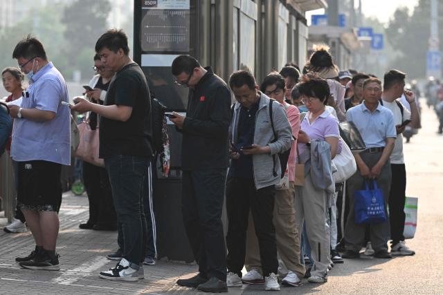 People wait for a bus half an hour before US President Donald Trump’s motorcade passed by on the way to a state banquet in Beijing on May 14, 2026. (Photo by GREG BAKER / AFP)