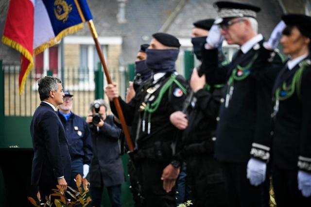 France's Justice Minister Gerald Darmanin (L) stands at attention during a wreath laying ceremony as he takes part in a visit marking the second anniversary of the 2024 Incarville attack, at the Pole de Rattachement dExtractions Judiciaires - PREJ (Judicial Extraction Coordination Centre) in Caen, north-western France on May 14, 2026. On May 14, 2024, a group of gunmen killed two prison officers and wounded three others, in an attack of a prison van transporting inmate Mohamed Amra at a motorway toll in Incarville, northern France. Amra's deadly escape marked a "turning point" in France, speeding up the introduction of new investigative tools and the construction of new prisons. However, investigators still face challenges in the face of a rapidly growing organised crime scene. (Photo by Lou BENOIST / AFP)