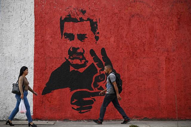 People walk past a mural depicting ousted Venezuelan President Nicolas Maduro flashing the V sign, in Caracas on May 14, 2026. (Photo by Federico PARRA / AFP)