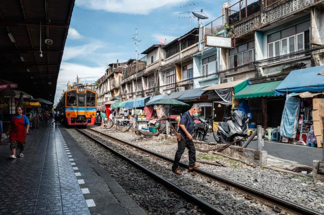 A man walks across the tracks as a SRT (State Railway of Thailand) train waits at the platform of Wongwian Yai Railway Station in Bangkok on May 14, 2026. (Photo by ANTHONY WALLACE / AFP)