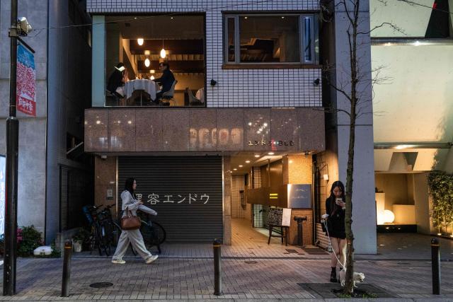 A couple eats in a restaurant as two women pass below on the street in Tokyo on May 14, 2026. (Photo by ANDREW CABALLERO-REYNOLDS / AFP)
