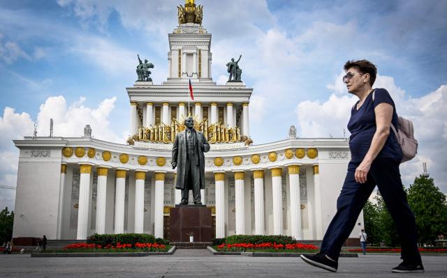 A woman walks by a monument to the Soviet Union founder Vladimir Lenin in front on the main building at the All-Russia Exhibition Centre (VDNKh) in Moscow on May 14, 2026. (Photo by Alexander NEMENOV / AFP)