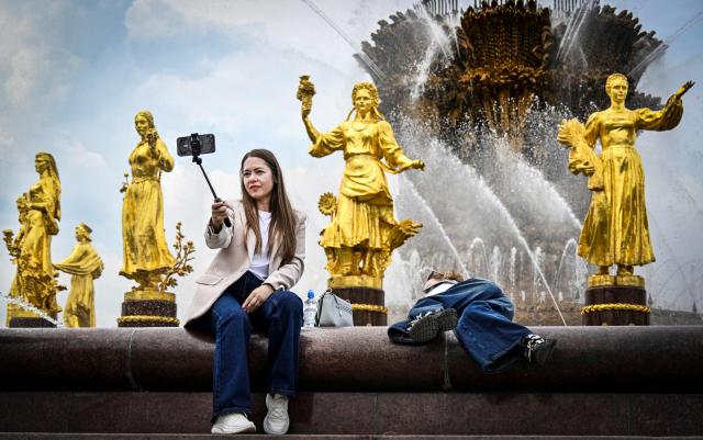 People have fun by the "Friendship of Nations" fountain at the All-Russia Exhibition Centre (VDNKh) in Moscow on May 14, 2026. The fountain was installed at the All-Russia Exhibition Centre (VDNKh), a trade show and amusement park, in 1954, with 16 gilded bronze sculptures of young women representing 16 republics of the USSR around the oval fountain bowl featuring a wheat sheaf. (Photo by Alexander NEMENOV / AFP)