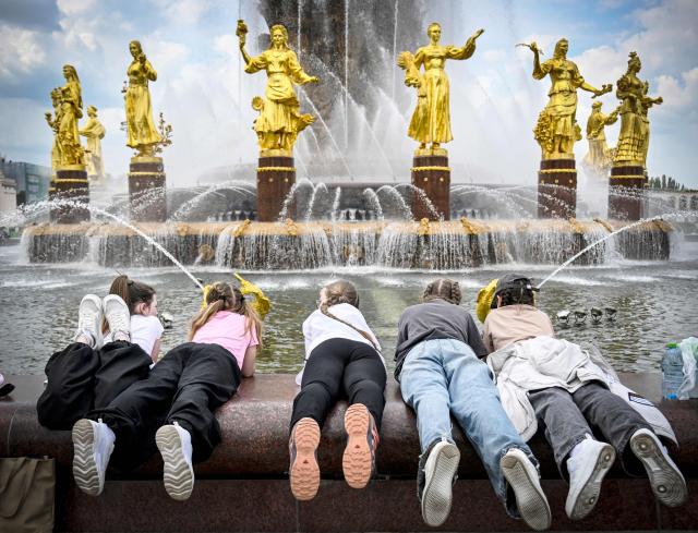 Children have fun by the "Friendship of Nations" fountain at the All-Russia Exhibition Centre (VDNKh) in Moscow on May 14, 2026. The fountain was installed at the All-Russia Exhibition Centre (VDNKh), a trade show and amusement park, in 1954, with 16 gilded bronze sculptures of young women representing 16 republics of the USSR around the oval fountain bowl featuring a wheat sheaf. (Photo by Alexander NEMENOV / AFP)
