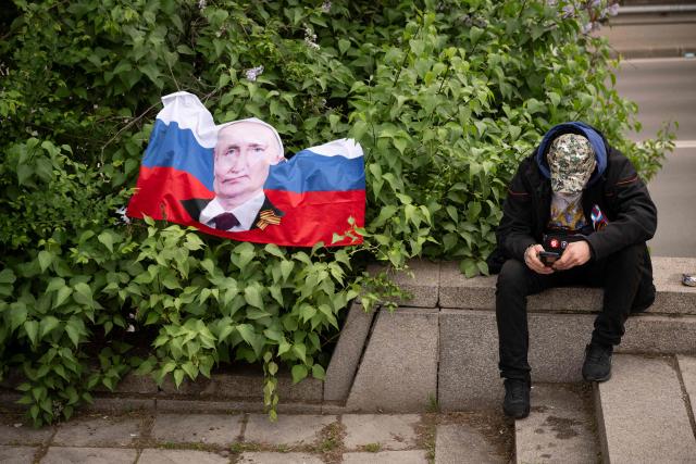 (FILES) A man sits next to a Russian flag with the portrait of Russian President Vladimir Putin during the celebration of the Victory Day marking the Allied victory against Nazi Germany and the end of World War II in Europe (VE Day), in Sofia, on May 9, 2026. Bulgaria's Rumen Radev won April's election with backing from traditional pro-Russian voters, but festivities commemorating the end of World War II showed he has not charmed all in the EU member historically close to Russia. (Photo by Nikolay DOYCHINOV / AFP)