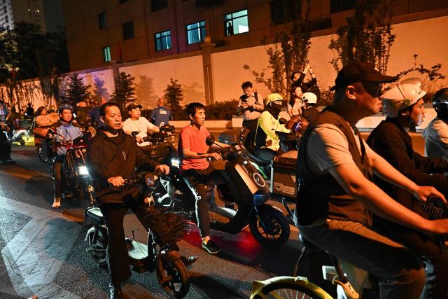People wait before the motorcade of US President Donald Trump passes by in Beijing on May 14, 2026. (Photo by Pedro PARDO / AFP)