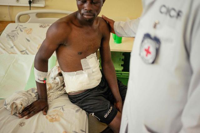 TOPSHOT - Tusenge Jean Claude, wounded during the bombing of the Mushaki market, is tended to by a doctor at the International Committee of the Red Cross (ICRC) supported CBCA Hospital in Goma on May 14, 2026. This father of six says he was injured while returning from the fields and stopping at the market to look for food. An explosion threw him to the ground, leaving shrapnel lodged in his body. 
He arrived at the hospital in a critical condition, weak and under medical care, but says he is now slowly recovering thanks to the treatment he has received. (Photo by Jospin Mwisha / AFP)