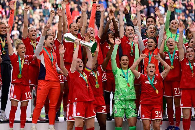 Bayern Munich's Icelandic defender #04 Glodis Viggosdottir (C-L, bottom) raises the trophy as Team FC Bayern Munich celebrates winning the Women's German Cup (DFB Pokal) Women's German Cup (DFB-Pokal) final football match between VfL Wolfsburg and FC Bayern Munich in Cologne, western Germany, on Mai 14, 2026. (Photo by INA FASSBENDER / AFP) / DFB REGULATIONS PROHIBIT ANY USE OF PHOTOGRAPHS AS IMAGE SEQUENCES AND QUASI-VIDEO.
