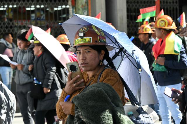 A woman miner uses her mobile phone during a march to demand the resignation of Bolivian President Rodrigo Paz in La Paz, on May 14, 2026. For the past two weeks, workers, farmers, school teachers, Indigenous groups and transport workers have been pressuring the government. Their demands range from wage increases and economic stabilization to opposition to the privatization of public companies. (Photo by AIZAR RALDES / AFP)