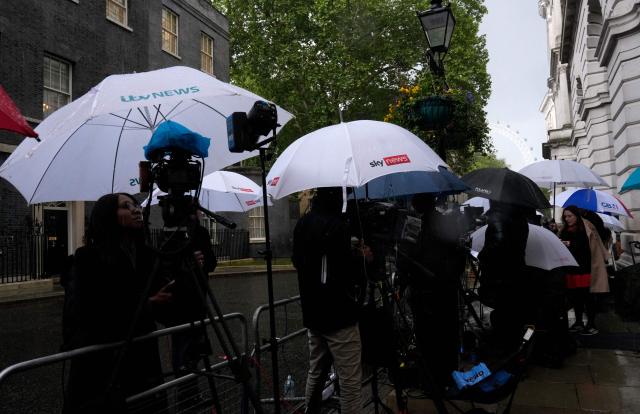 Members of the media, including ITV news, Sky News, and GB News, shelter from the rain as they work outside Number 10 Downing Street in central London on May 14, 2026. Britain's health minister Wes Streeting resigned Thursday while Greater Manchester mayor Andy Burnham unveiled a bid to return to parliament, as political manoeuvring increased to oust Prime Minister Keir Starmer. (Photo by CARLOS JASSO / AFP)