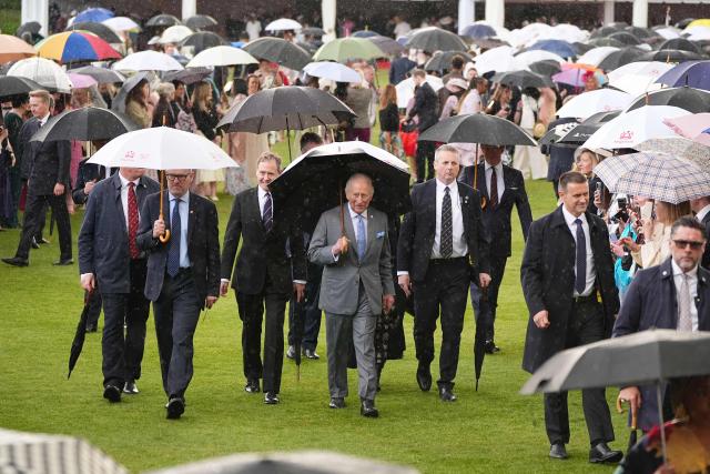 Britain's King Charles III shelters from the rain bebath an umbrella during a Royal Garden Party at Buckingham Palace, in London, on May 14, 2026, celebrating the 50th Anniversary of the King’s Trust. (Photo by Aaron Chown / POOL / AFP)