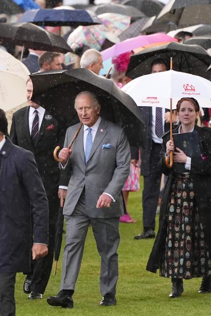 Britain's King Charles III shelters from the rain bebath an umbrella during a Royal Garden Party at Buckingham Palace, in London, on May 14, 2026, celebrating the 50th Anniversary of the King’s Trust. (Photo by Aaron Chown / POOL / AFP)