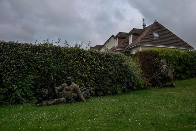 A French Foreign Legion paratrooper from the 2nd Foreign Parachute Regiment (2e REP) sits against a garden hedge without his helmet, indicating he has been declared a simulated casualty, as a comrade holds position nearby during a urban assault exercise in La Souterraine, central France, on May 14, 2026. The exercise, running from May 11 to 20 across Nouvelle-Aquitaine and Centre-Val de Loire, tests short-notice redeployment and interoperability between air and ground components  capabilities central to France's contribution to NATO rapid-reaction forces. (Photo by Philippe LOPEZ / AFP)