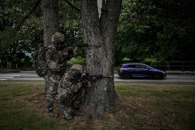 French Foreign Legion paratroopers from the 2nd Foreign Parachute Regiment (2e REP) take up firing positions behind trees as a civilian car passes on the road behind them during a urban assault exercise in La Souterraine, central France, on May 14, 2026. The exercise, running from May 11 to 20 across Nouvelle-Aquitaine and Centre-Val de Loire, tests short-notice redeployment and interoperability between air and ground components  capabilities central to France's contribution to NATO rapid-reaction forces. (Photo by Philippe LOPEZ / AFP)