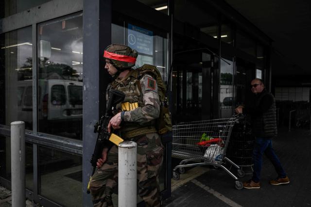 A French Foreign Legion paratrooper from the 2nd Foreign Parachute Regiment (2e REP) holds a position outside a supermarket as a civilian shopper passes by during a urban combat exercise in La Souterraine, central France, on May 14, 2026. The exercise, running from May 11 to 20 across Nouvelle-Aquitaine and Centre-Val de Loire, tests short-notice redeployment and interoperability between air and ground components — capabilities central to France's contribution to NATO rapid-reaction forces. (Photo by Philippe LOPEZ / AFP)