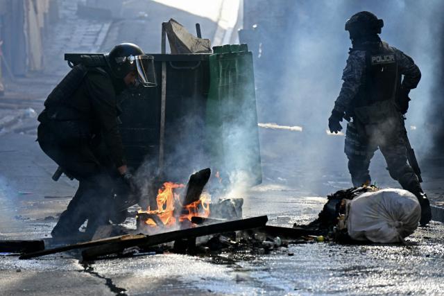 A riot police officer attemps to extinguish a fire as clashes erupted with miners during a march to demand the resignation of Bolivian President Rodrigo Paz, in La Paz, on May 14, 2026. For the past two weeks, workers, farmers, school teachers, Indigenous groups and transport workers have been pressuring the government. Their demands range from wage increases and economic stabilization to opposition to the privatization of public companies. (Photo by AIZAR RALDES / AFP)