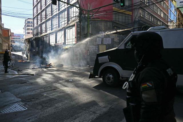 A riot police vehicle sprays water to extinguish a fire as clashes erupted with miners during a march to demand the resignation of Bolivian President Rodrigo Paz, in La Paz, on May 14, 2026. For the past two weeks, workers, farmers, school teachers, Indigenous groups and transport workers have been pressuring the government. Their demands range from wage increases and economic stabilization to opposition to the privatization of public companies. (Photo by AIZAR RALDES / AFP)