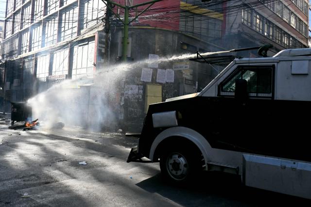 A riot police vehicle sprays water to extinguish a fire as clashes erupted with miners during a march to demand the resignation of Bolivian President Rodrigo Paz, in La Paz, on May 14, 2026. For the past two weeks, workers, farmers, school teachers, Indigenous groups and transport workers have been pressuring the government. Their demands range from wage increases and economic stabilization to opposition to the privatization of public companies. (Photo by AIZAR RALDES / AFP)