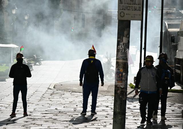 Miners stand in front of tear gas as clashes erupted with miners during a march to demand the resignation of Bolivian President Rodrigo Paz, in La Paz, on May 14, 2026. For the past two weeks, workers, farmers, school teachers, Indigenous groups and transport workers have been pressuring the government. Their demands range from wage increases and economic stabilization to opposition to the privatization of public companies. (Photo by AIZAR RALDES / AFP)