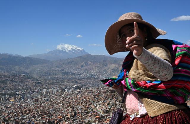 An indigenous woman walks past with the snow-capped Illimani mountain on the background in La Paz on May 14, 2026. (Photo by Aizar RALDES / AFP)