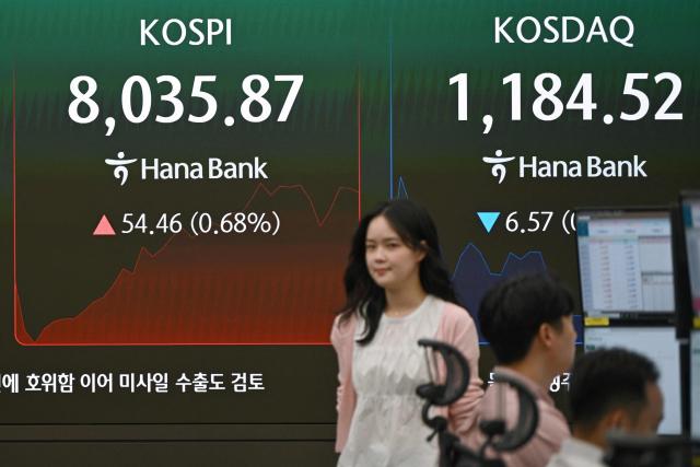 A currency dealer walks past a screen showing South Korea's benchmark stock index (KOSPI) as it breaks 8,000 points in a foreign exchange dealing room at the Hana Bank headquarters in Seoul on May 15, 2026. South Korea's benchmark Kospi index topped 8,000 points for the first time on May 15, buoyed by an artificial intelligence-driven boom in the country's semiconductor industry. (Photo by Jung Yeon-je / AFP)