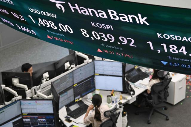 Currency dealers monitor exchange rates as a screen shows South Korea's benchmark stock index (KOSPI) surpassing 8,000 points in a foreign exchange dealing room at the Hana Bank headquarters in Seoul on May 15, 2026. South Korea's benchmark Kospi index topped 8,000 points for the first time on May 15, buoyed by an artificial intelligence-driven boom in the country's semiconductor industry. (Photo by Jung Yeon-je / AFP)