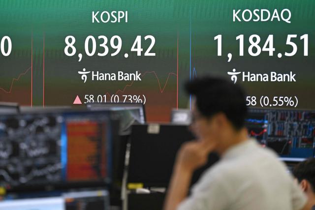 A currency dealer monitors exchange rates as a screen shows South Korea's benchmark stock index (KOSPI) surpassing 8,000 points in a foreign exchange dealing room at the Hana Bank headquarters in Seoul on May 15, 2026. South Korea's benchmark Kospi index topped 8,000 points for the first time on May 15, buoyed by an artificial intelligence-driven boom in the country's semiconductor industry. (Photo by Jung Yeon-je / AFP)