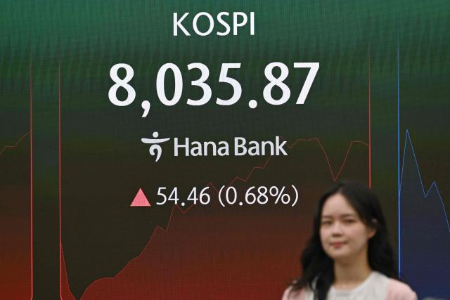 A currency dealer walks past a screen showing South Korea's benchmark stock index (KOSPI) as it breaks 8,000 points in a foreign exchange dealing room at the Hana Bank headquarters in Seoul on May 15, 2026. South Korea's benchmark Kospi index topped 8,000 points for the first time on May 15, buoyed by an artificial intelligence-driven boom in the country's semiconductor industry. (Photo by Jung Yeon-je / AFP)