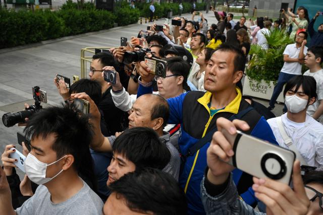 People take photos as US President Donald Trump’s motorcade departs a hotel on the way to a meeting with China’s President Xi Jinping in Beijing on May 15, 2026. (Photo by GREG BAKER / AFP)