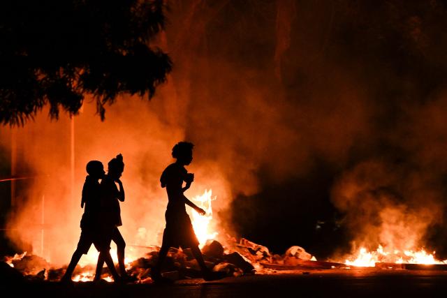 People walk past a fire set by demonstrators during a protest against the lack of energy and blackouts in the Lawton neighborhood in Havana on May 14, 2026. Cuba blamed the United States for the "particularly tense" situation in its electricity grid, as the east of the country was hit by another widespread power cut on May 14, 2026. Washington has once again offered $100 million in aid, which the island’s government is "willing" to consider. (Photo by Yamil LAGE / AFP)