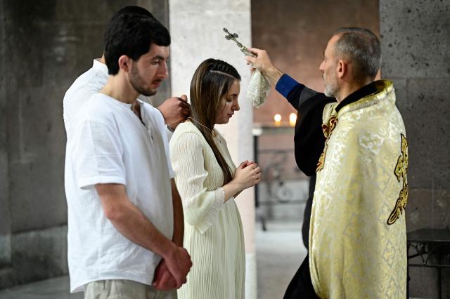 A priest baptizing a young woman in Echmiadzin, Armenia's ancient spiritual centre and the seat of the leader of the Armenian Apostolic Church, outside Yerevan, on April 18, 2026. (Photo by KAREN MINASYAN / AFP)