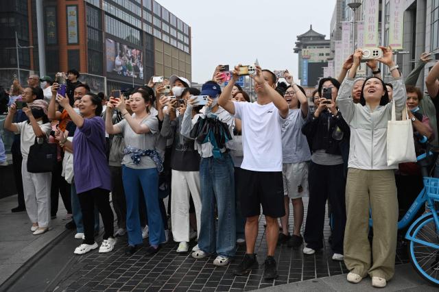 People take photos as US President Donald Trump’s motorcade passes the Wangfujing shopping street on the way to the airport after Trump met with China’s President Xi Jinping in Beijing on May 15, 2026. (Photo by GREG BAKER / AFP)