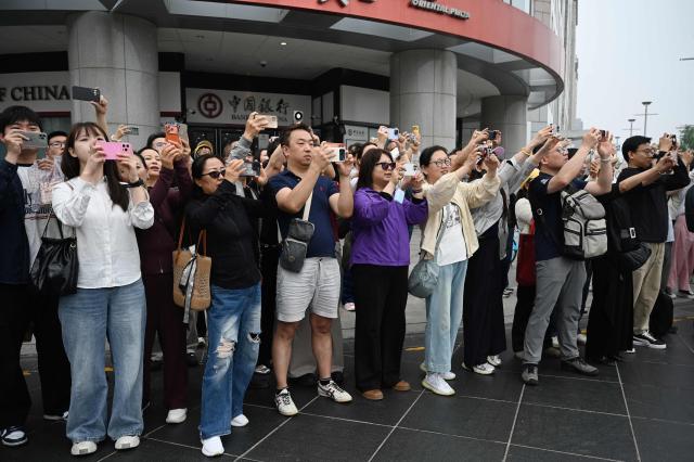 People take photos as US President Donald Trump’s motorcade passes the Wangfujing shopping street on the way to the airport after Trump met with China’s President Xi Jinping in Beijing on May 15, 2026. (Photo by GREG BAKER / AFP)