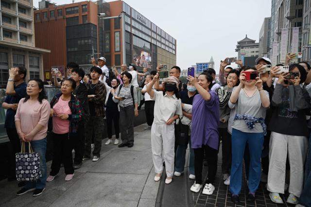 People take photos as US President Donald Trump’s motorcade passes the Wangfujing shopping street on the way to the airport after Trump met with China’s President Xi Jinping in Beijing on May 15, 2026. (Photo by GREG BAKER / AFP)
