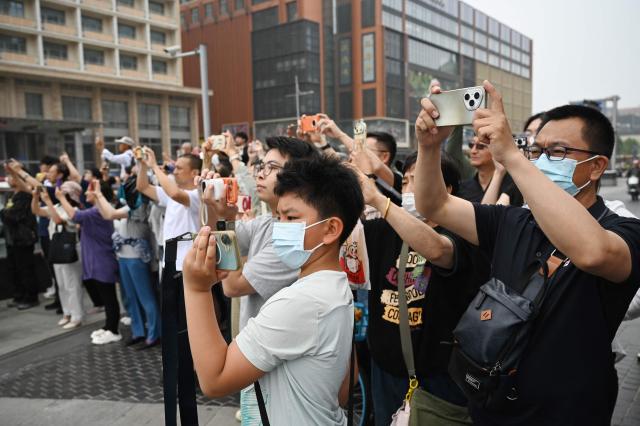 People take photos as US President Donald Trump’s motorcade passes the Wangfujing shopping street on the way to the airport after Trump met with China’s President Xi Jinping in Beijing on May 15, 2026. (Photo by GREG BAKER / AFP)