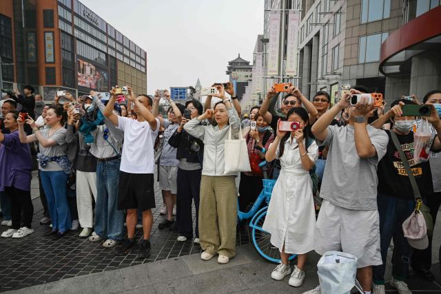 People take photos as US President Donald Trump’s motorcade passes the Wangfujing shopping street on the way to the airport after Trump met with China’s President Xi Jinping in Beijing on May 15, 2026. (Photo by GREG BAKER / AFP)