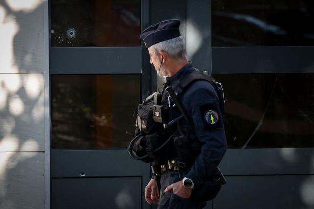 A police officer walks past the front door of a building with bullet holes that was the scene of a shooting in Nantes, western France, on May 15, 2026, where a 15-year-old was killed and two minors were injured. A teenager of about fifteen was shot and killed on the evening of May 14, and two other minors were wounded in a working-class neighborhood of Nantes, which had already been hit by deadly shootings linked to drug trafficking at the end of April. The shooting occurred around 7:30 p.m. in an apartment building, and the suspected shooters, who arrived on a motorcycle, fled the scene, according to multiple sources close to the investigation. The deceased teenager was shot in the heart, these sources confirmed. The two wounded teenagers, who were taken to the hospital, are not in life-threatening condition, according to a source close to the investigation. They are reportedly 13 and 14 years old. (Photo by FRED TANNEAU / AFP)