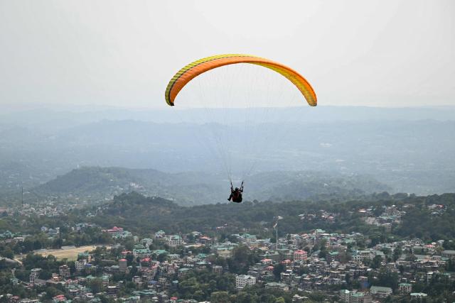 A man paraglides against the backdrop of the city's skyline in Dharamsala on May 15, 2026. (Photo by Sajjad HUSSAIN / AFP)