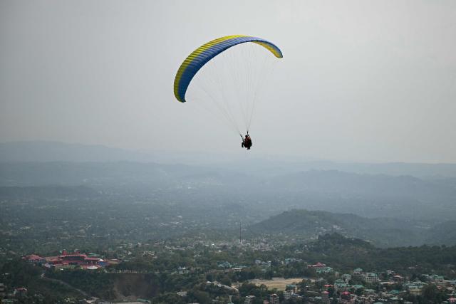 A man paraglides against the backdrop of the city's skyline in Dharamsala on May 15, 2026. (Photo by Sajjad HUSSAIN / AFP)