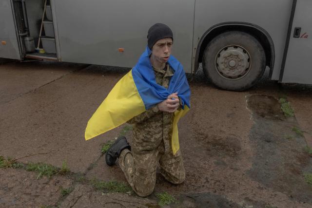A released Ukrainian prisoner of war (POW) wrapped with a national flag kneels down following a prisoner exchange at an undisclosed location, in the Chernihiv region on May 15, 2026, amid the Russian invasion of Ukraine. Russia and Ukraine exchanged 205 prisoners of war each on May 15, Moscow and Kyiv said, a week after US President Donald Trump announced a large swap would take place between the warring sides. (Photo by Roman PILIPEY / AFP)