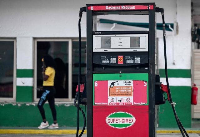 A woman walks past an empty petrol station in Havana on May 15, 2026. From May 15, Cuba is implementing variable pricing for fuel sold in foreign currency, a measure aimed at addressing rising import costs. Prices at service stations may now fluctuate based on factors such as suppliers, freight, supply routes, insurance and global market volatility, meaning different prices may coexist across the country depending on operational costs. (Photo by YAMIL LAGE / AFP)