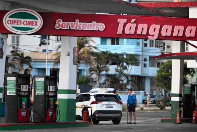 Men chat at an empty petrol station in Havana on May 15, 2026. From May 15, Cuba is implementing variable pricing for fuel sold in foreign currency, a measure aimed at addressing rising import costs. Prices at service stations may now fluctuate based on factors such as suppliers, freight, supply routes, insurance and global market volatility, meaning different prices may coexist across the country depending on operational costs. (Photo by YAMIL LAGE / AFP)