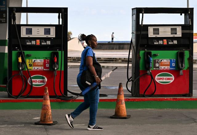 A woman walks past an empty petrol station in Havana on May 15, 2026. From May 15, Cuba is implementing variable pricing for fuel sold in foreign currency, a measure aimed at addressing rising import costs. Prices at service stations may now fluctuate based on factors such as suppliers, freight, supply routes, insurance and global market volatility, meaning different prices may coexist across the country depending on operational costs. (Photo by YAMIL LAGE / AFP)