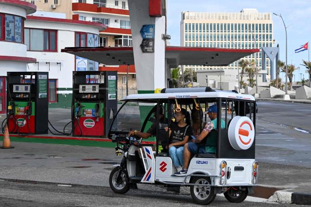 An electric tricycle drives past an empty petrol station in Havana on May 15, 2026. From May 15, Cuba is implementing variable pricing for fuel sold in foreign currency, a measure aimed at addressing rising import costs. Prices at service stations may now fluctuate based on factors such as suppliers, freight, supply routes, insurance and global market volatility, meaning different prices may coexist across the country depending on operational costs. (Photo by YAMIL LAGE / AFP)