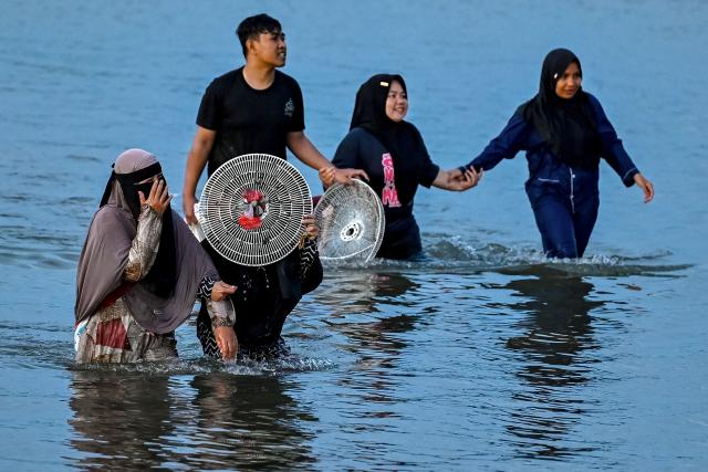 People wade through shallow waters after catching shellfish at a beach in Banda Aceh on May 15, 2026. (Photo by Chaideer MAHYUDDIN / AFP)