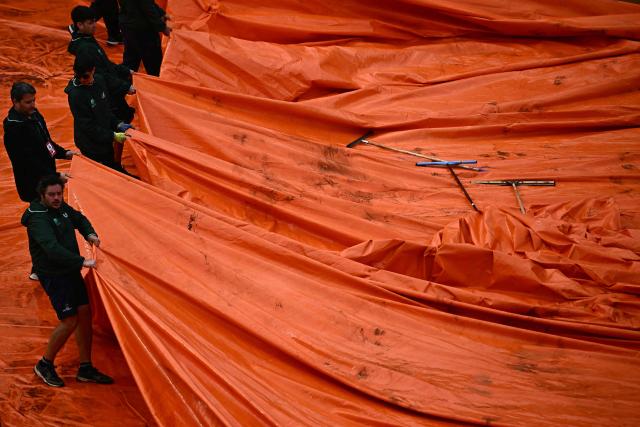 Staff remove the tarp from the clay court after the semi-final match between Italy's Luciano Darderi and Norway's Casper Ruud was interrupted due to a storm during the ATP Rome Open tennis tournament at Foro Italico in Rome on May 15, 2026. (Photo by Filippo MONTEFORTE / AFP)