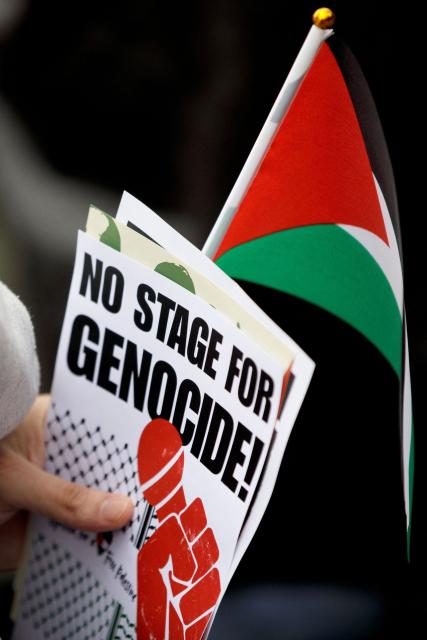 A participant holds a leaflet with the lettering 'No stage for genocide' and a Palestinian flag during a pro-Palestinian demonstration under the motto 'Song Protest Vienna 2026 - No Stage for Genocide' against Israel's participation in the Eurovision Song Contest (ESC), in front of the Maria Theresa Monument in Vienna, Austria, on May 15, 2026. (Photo by Alex HALADA / AFP)