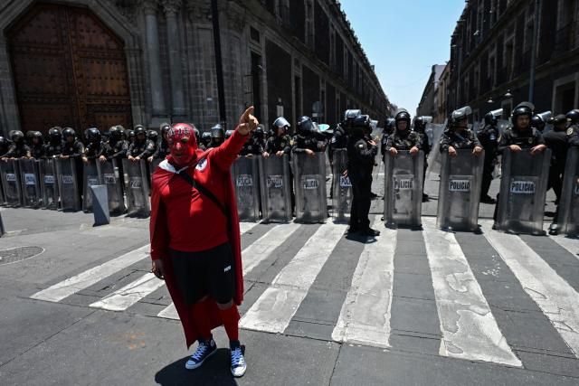A teacher, a member of the National Coordinator of Education Workers (CNTE), wears a mask as he takes part in a protest march in front of a line of riot police, in Mexico City, on May 15, 2026. (Photo by Yuri CORTEZ / AFP)
